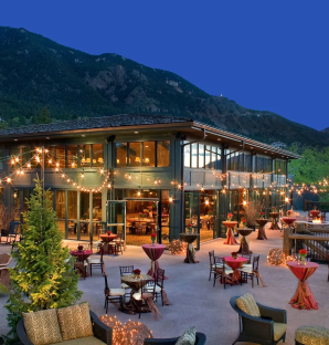 A House With A Pool And A Patio With Tables And Chairs And A Hill In The Background