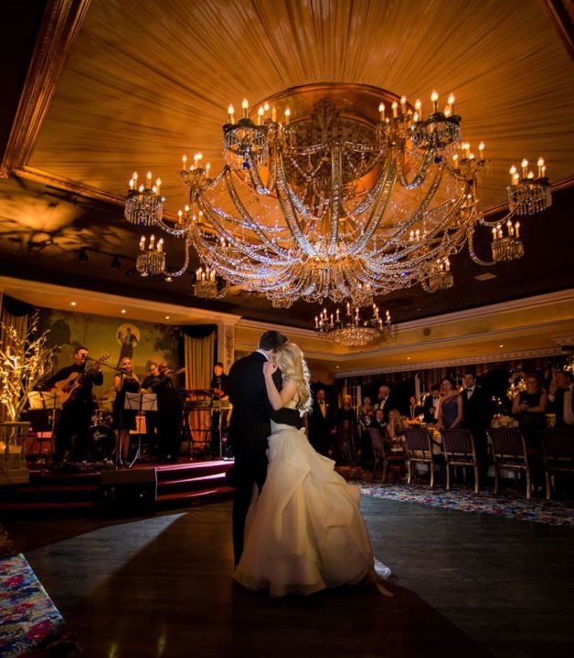 A Man And Woman Dancing In A Room With Chandeliers And A Large Chandelier