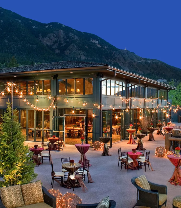 A House With A Pool And A Patio With Tables And Chairs And A Hill In The Background