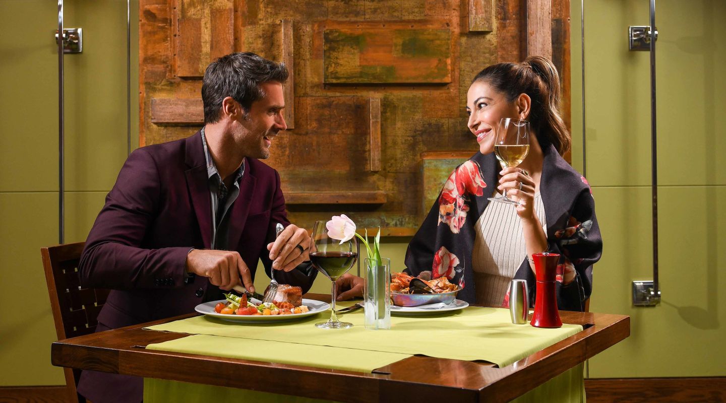 A Man And Woman Sitting At A Table With Food